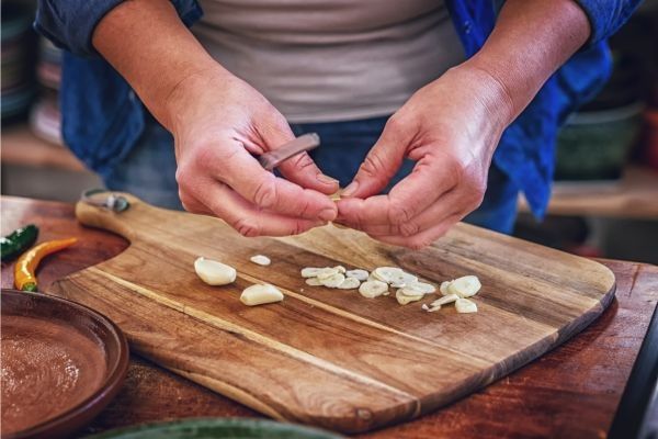 Mujer cortando ajo en rodajas sobre tabla de madera