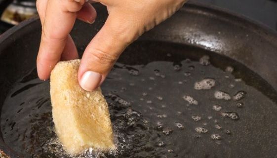 Mano poniendo croqueta en la sartén para freir