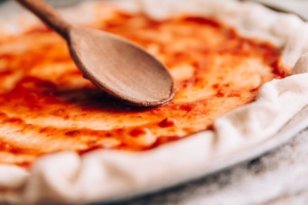 Cuchara de madera extendiendo la salsa de tomate sobre la masa de la pizza