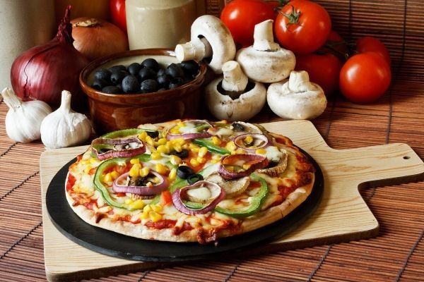 Pizza vegana en tabla de madera junto a varios ingredientes