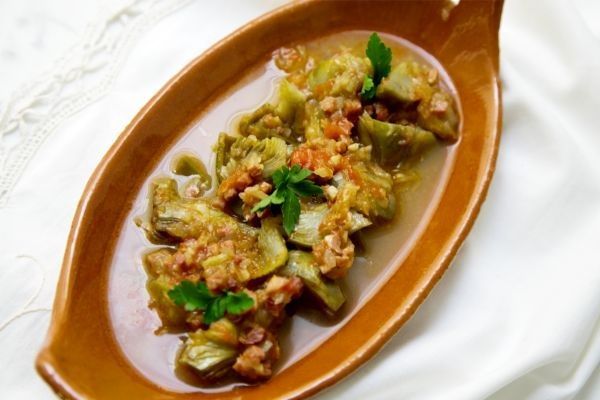 Alcachofas con jamón presentadas en plato de barro