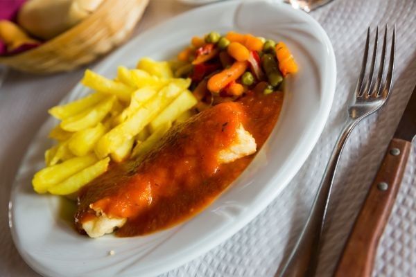 Bacalao a la vizcaína presentado en plato blanco junto a patatas fritas y verduras