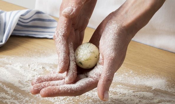 Manos haciendo bolitas con la masa de buñuelos de bacalao