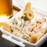 Ensaladilla rusa presentada en tapa con aceitunas y picos