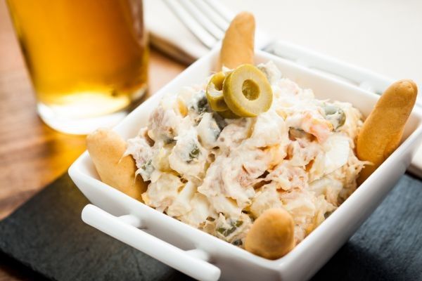 Ensaladilla rusa presentada en tapa con aceitunas y picos
