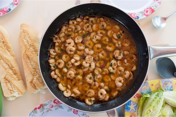 Gambas al pil pil presentadas en sartén junto a dos barras de pan