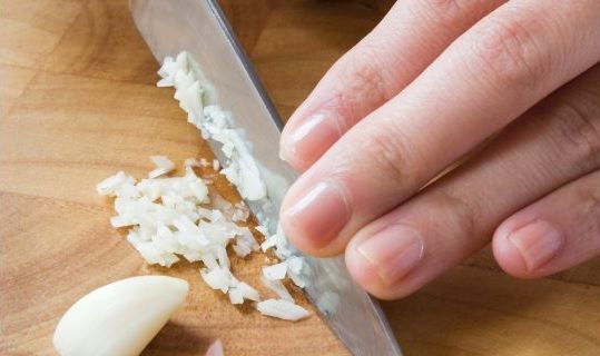 Mano picando ajo con cuchillo sobre tabla de madera