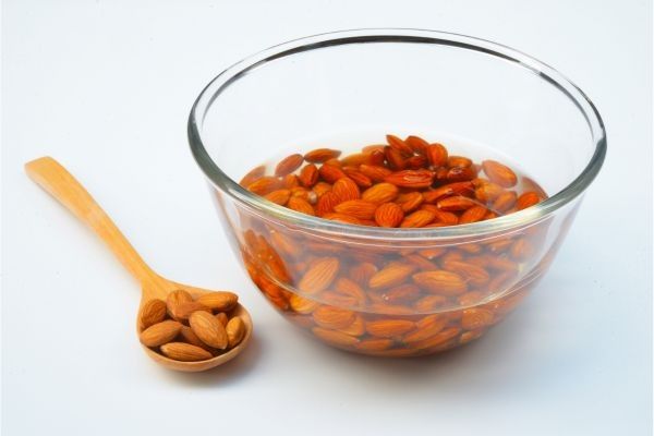 Almendras crudas en recipiente de vidrio con agua y cuchara de madera
