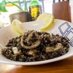 Arroz negro con calamares presentado en plato blanco con limón decorando en el borde