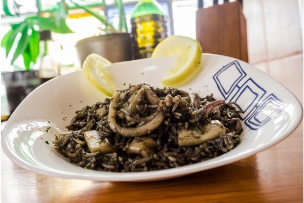 Arroz negro con calamares presentado en plato blanco con limón decorando en el borde