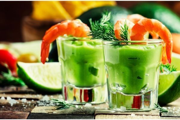 Cóctel de gambas con aguacate y lima presentados en vasos individuales junto a rodajas de lima