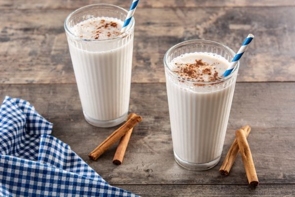 Leche merengada presentada en vasos con pajitas y canela en rama