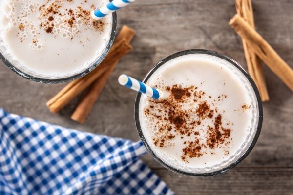 Vasos con leche merengada espolvoreados con canela y decorados alrededor con canela en rama