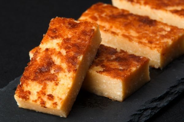 Quesada pasiega cortada en trozos y presentada sobre plato de pizarra negra