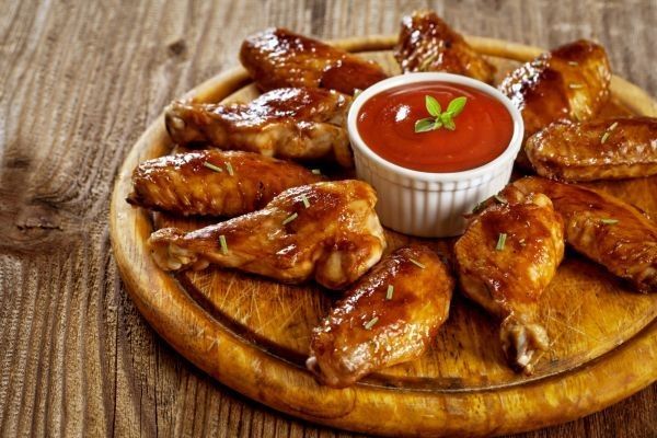 Alitas de pollo picantes Buffalo wings presentadas en tabla de madera junto a salsa