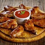 Alitas de pollo picantes al estilo Buffalo wings presentadas en tabla de madera junto a salsa