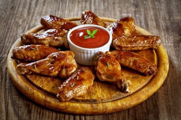 Alitas de pollo picantes al estilo Buffalo wings presentadas en tabla de madera junto a salsa