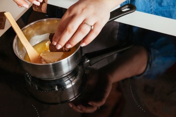 Chef derritiendo chocolate y mantequilla en un cazo en la vitrocerámica