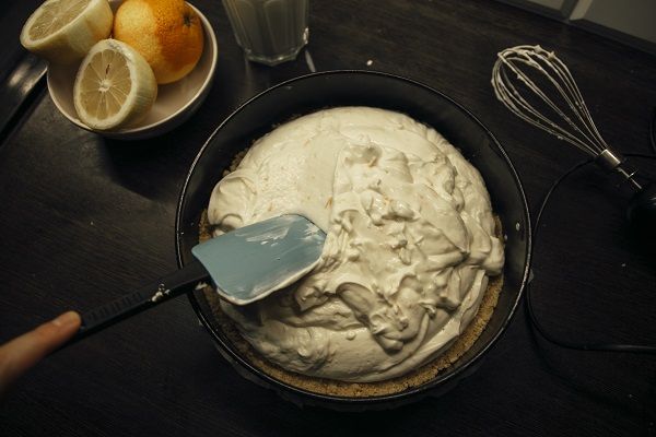 Chef extendiendo la masa de queso y nata con una espátula sobre la base de galletas