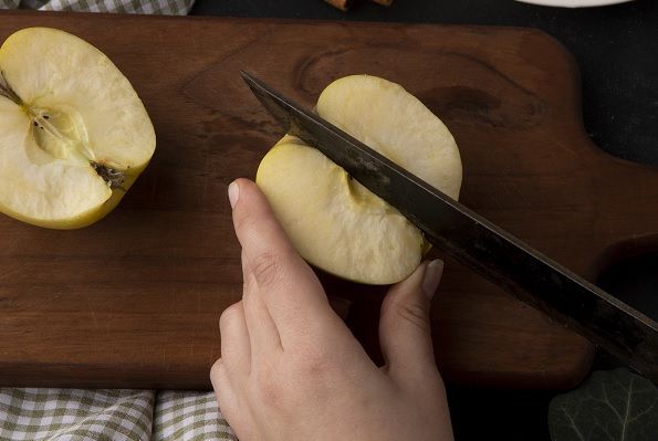 Chef cortando una manzana con cuchillo en tabla de madera