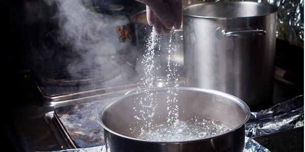 Mano echando sal a una olla con agua hirviendo