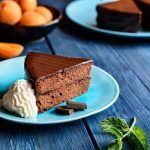 Tarta Sacher presentada en plato azul junto a nata, chocolate y melocotones