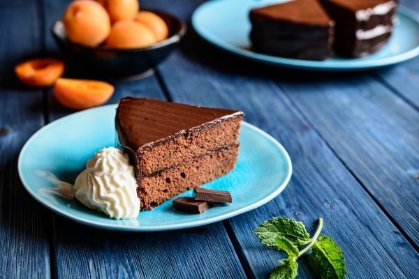 Tarta Sacher presentada en plato azul junto a nata, chocolate y melocotones
