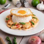 Arroz con huevo frito y pollo presentado en plato blanco y con ingredientes alrededor