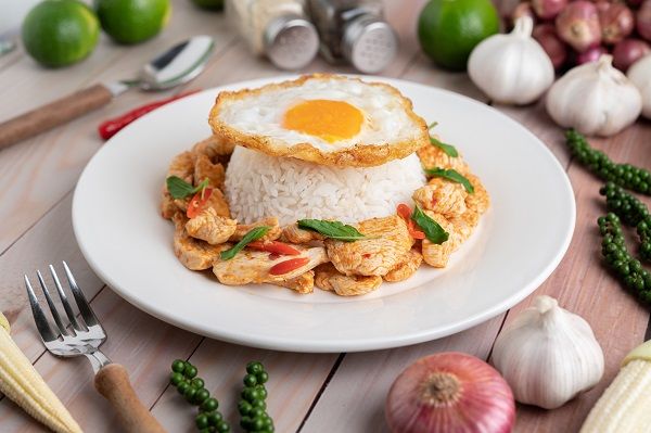Arroz con huevo frito y pollo presentado en plato blanco y con ingredientes alrededor
