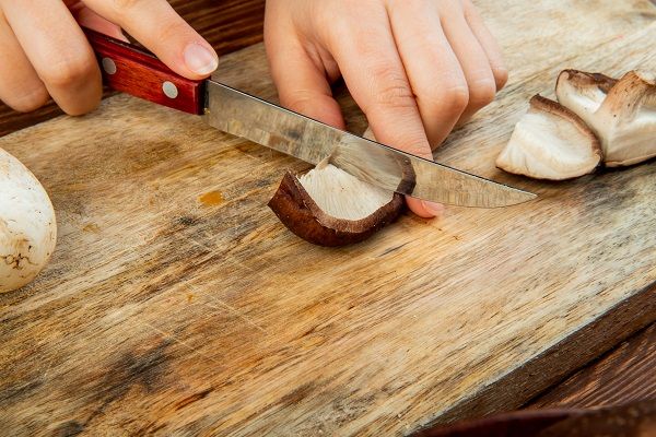 Chef cortando boletus edulis sobre tabla de madera con cuchillo