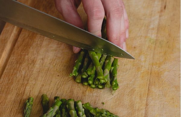 Chef cortando espárragos verdes trigueros en una tabla de madera