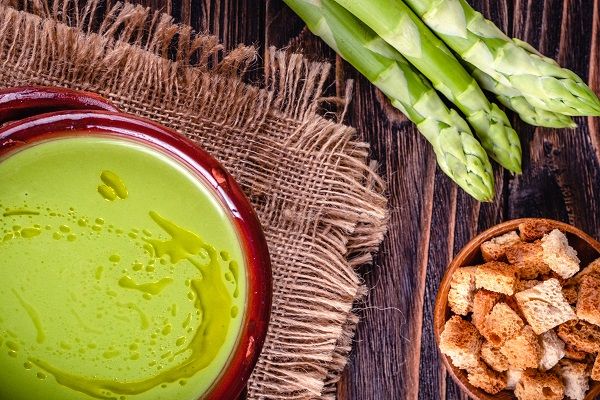 Crema de espárragos verdes presentada en cuenco de barro junto a unos espárragos trigueros y unos crutones