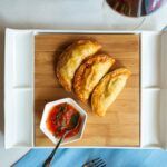 Empanadillas de atún al horno sobre tabla de madera junto a deliciosa salsa