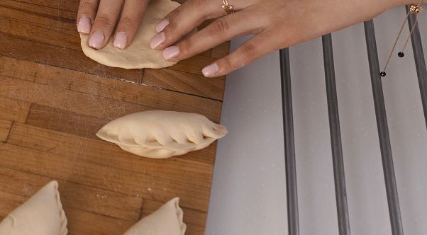 Manos de chef preparando empanadillas de atún sobre tabla de madera