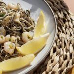 Gulas al ajillo con gambas presentadas en plato con rodajas de limón