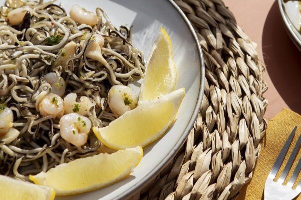 Gulas al ajillo con gambas presentadas en plato con rodajas de limón