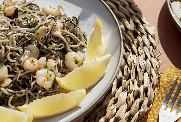 Gulas al ajillo con gambas presentadas en plato con rodajas de limón
