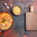 Fideos a la cazuela con carne presentados junto tabla de madera y ajos