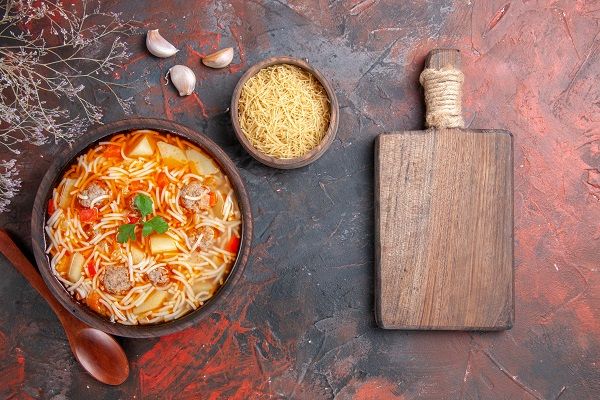 Fideos a la cazuela con carne presentados junto tabla de madera y ajos