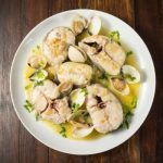 Merluza a la marinera con almejas presentada en plato blanco