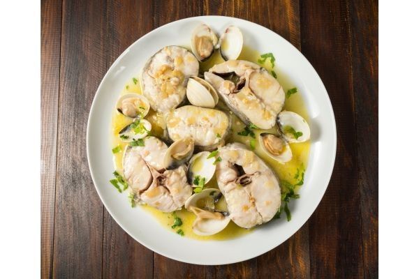 Merluza a la marinera con almejas presentada en plato blanco
