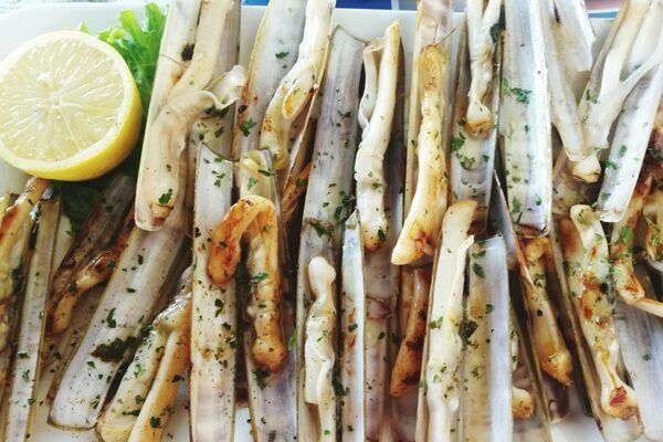 Navajas a la plancha con ajo y perejil presentadas junto a un limón