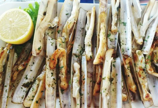 Navajas a la plancha con ajo y perejil presentadas junto a un limón