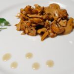 Níscalos al ajillo presentados en plato blanco con unas gotas de aceite y perejil