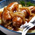 Salchichas al vino presentadas en plato de cerámica con puré de patatas