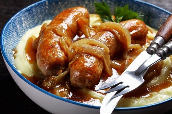 Salchichas al vino presentadas en plato de cerámica con puré de patatas