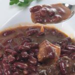 Alubias de Tolosa tradicional con sacramentos presentadas en plato blanco y con cuchara