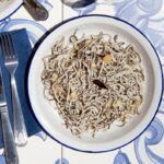Angulas a la bilbaína presentadas en plato blanco junto a cuchillo y tenedor con ajo cortado