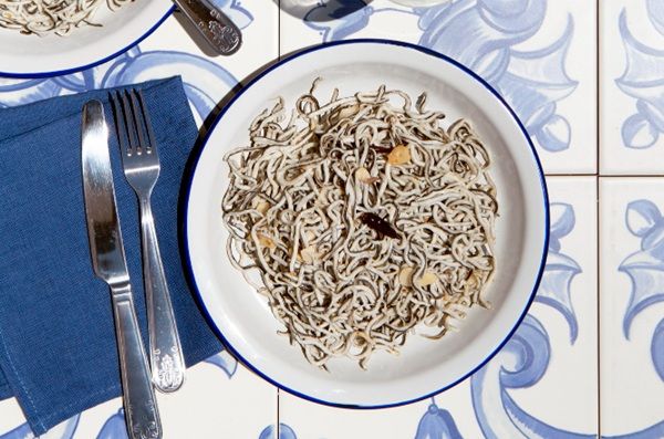 Angulas a la bilbaína presentadas en plato blanco junto a cuchillo y tenedor con ajo cortado