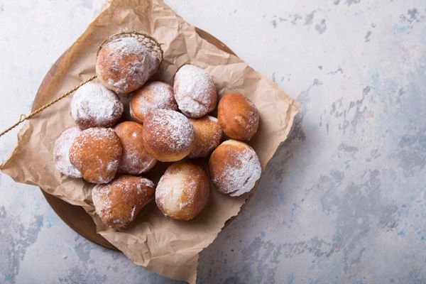Buñuelos dulces tradicionales presentados sobre papel marrón con una espumadera cogiendo uno